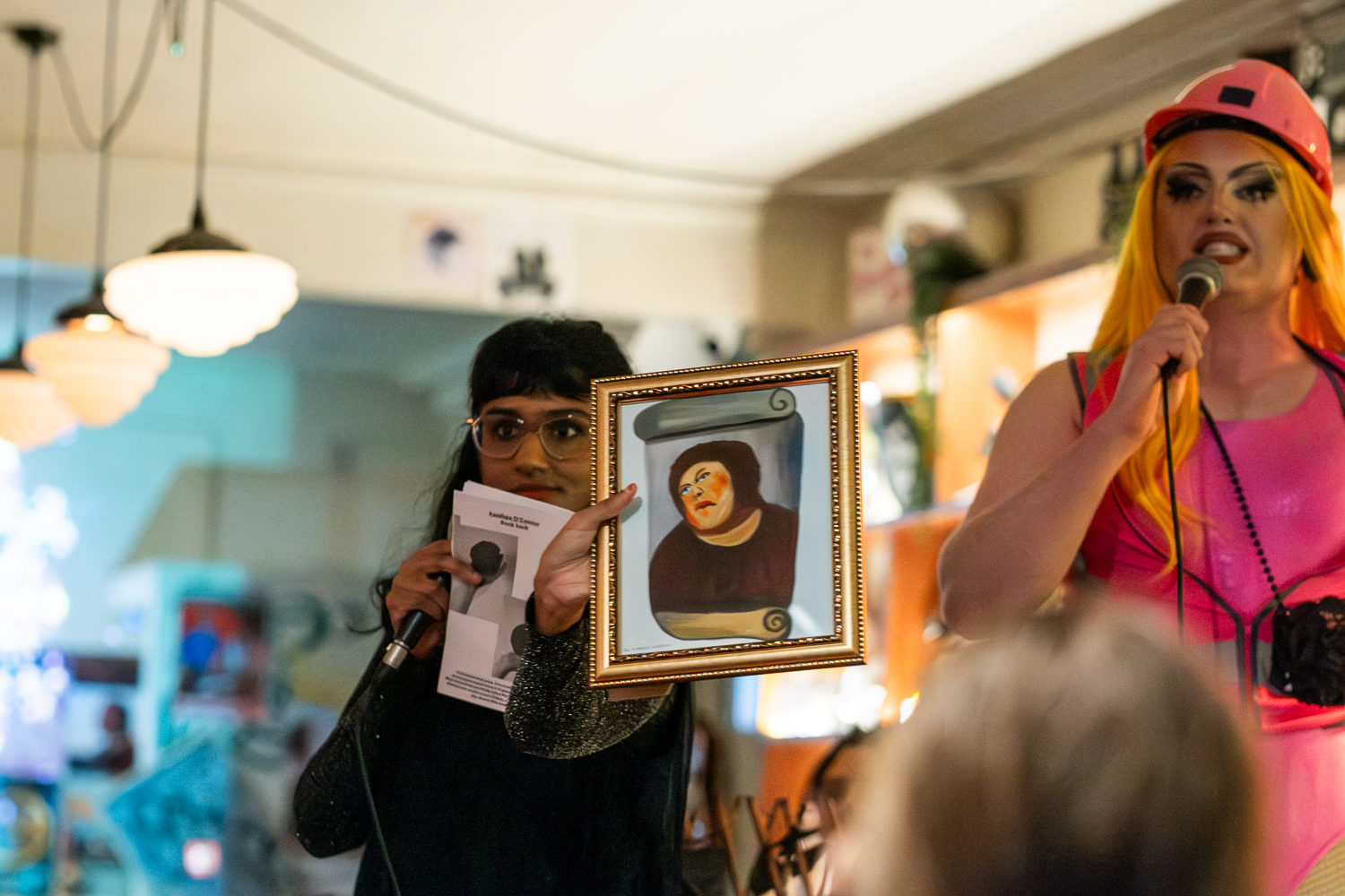 Comedian Vidya Rajan holding a parody painting at the Gina Rinehart comedy art auctionn (2024)